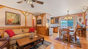 Una sala de estar acogedora con ventilador de techo de madera, un sofá, una mesa de centro y un comedor con mesa y sillas de madera.