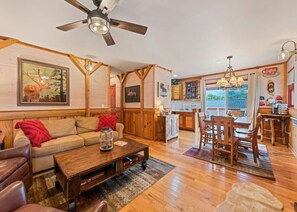 A cozy living room with a wooden ceiling fan, a sofa, a coffee table, and a dining area with a wooden table and chairs. - Maggie’s Mountain View-Breathtaking Views! Hot Tub (Maggie Valley)