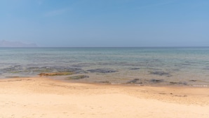 Ein Strand mit klarem Wasser, fernen Bergen und einem sandigen Ufer.