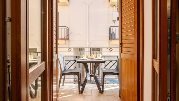 Eine offene Tür, die auf einen Balkon mit einem Tisch für zwei Personen, Stühlen und Blick ins Innere des Gebäudes führt.