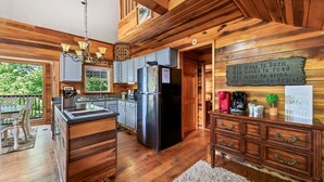Una cocina amplia con armarios de madera, un refrigerador de acero inoxidable y una isla de madera. Hay un cartel en la pared que dice 'Bienvenidos a nuestro hogar'.