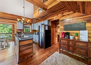 A spacious kitchen with wooden cabinetry, a stainless steel refrigerator, and a wooden island. There is a sign on the wall that reads "Welcome to our home." - Cubby Bear Cabin-Peaceful, Pet Friendly Great View (Maggie Valley)