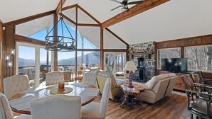 Ein geräumiges Wohnzimmer mit einer großen Holzbalkendecke, einem Essbereich mit weiß gepolsterten Stühlen und einem Steinkamin.