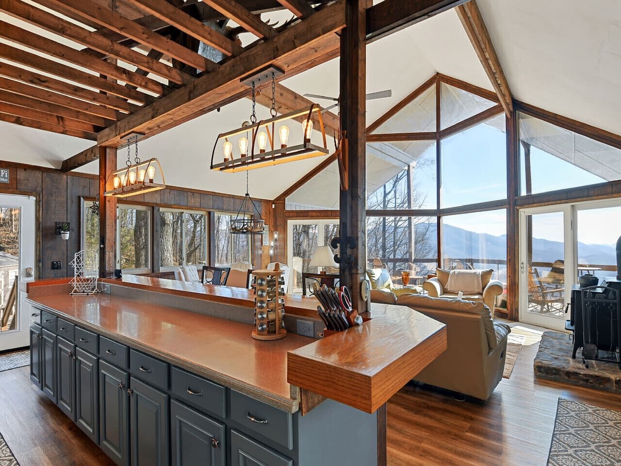 A spacious kitchen with a large island, wooden ceiling beams, and large windows offering a view of the outdoors.