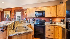 A kitchen with wooden cabinets, a black stove, a microwave, and a sink. - Mountain Laurel-Secluded Beauty + Majestic Views! (Maggie Valley)