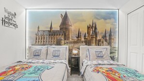 Ein Schlafzimmer mit zwei Betten, jedes mit einer Bettdecke und Kissenbezügen im Hogwarts-Design. An der Wand hinter den Betten befindet sich ein großes Wandbild des Hogwarts-Schlosses.
