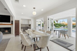 A modern kitchen with white cabinets, a dining area with a long table and patterned chairs, and a view of a pool outside. - "La Veranda" a Movie Colony Palm Springs Resort Pool and View Home, #069334 (Palm Springs)