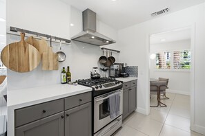 A modern kitchen with a gas stove, oven, and hanging pots. There are wooden cutting boards and a bottle of olive oil on the counter. - "La Veranda" a Movie Colony Palm Springs Resort Pool and View Home, #069334 (Palm Springs)