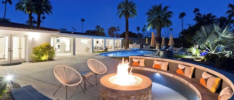 A well-lit outdoor area with a stone fire pit, seating, and a pool.