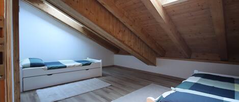 Une chambre mansardée avec de hauts plafonds, une lucarne, des poutres en bois et un lit blanc.