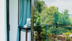 Un balcón con puerta corrediza de vidrio, una mesita con taza y platillo, y vistas a exuberante vegetación.
