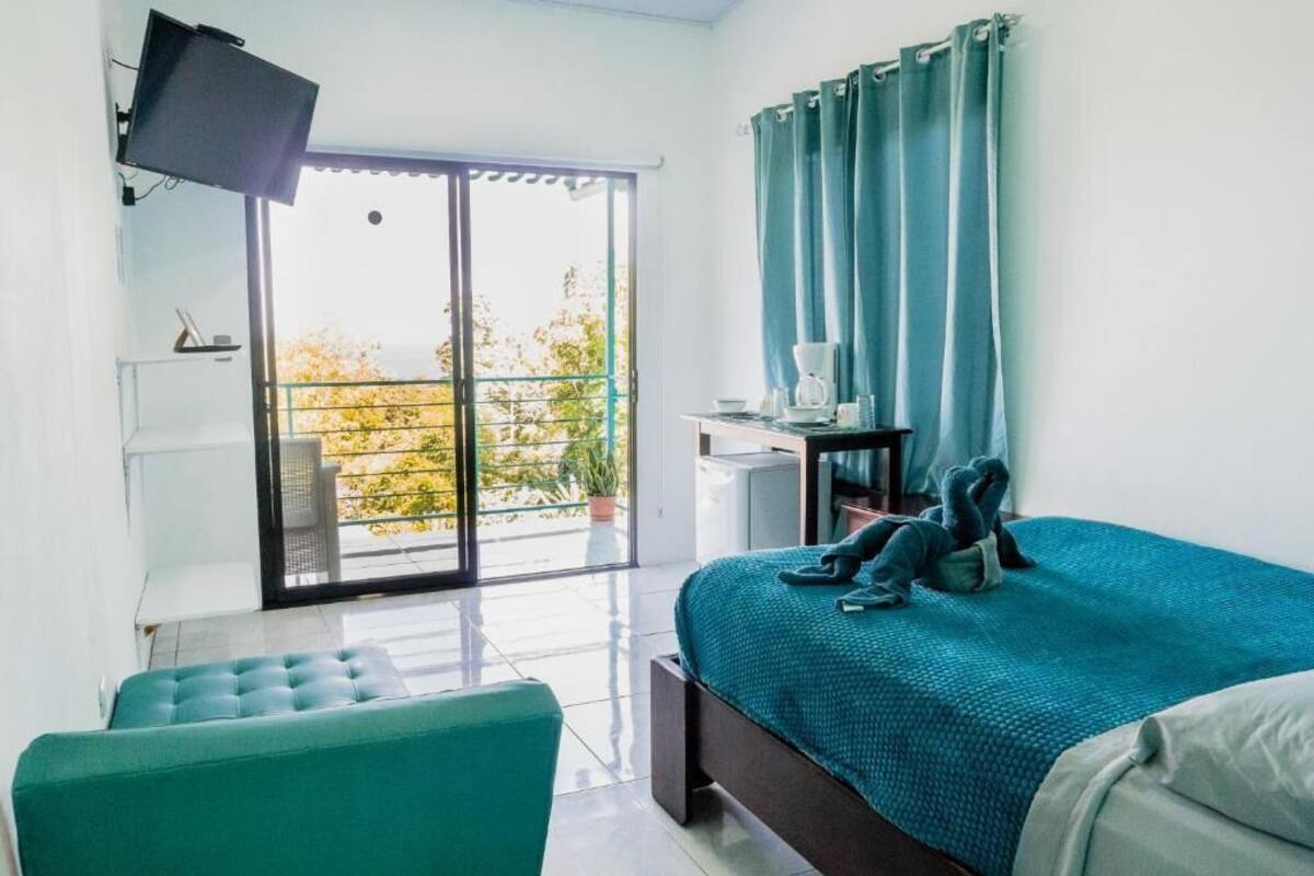 Un dormitorio moderno con una cama grande, un televisor de pantalla plana en la pared, un escritorio con una silla y un balcón con vistas a árboles.