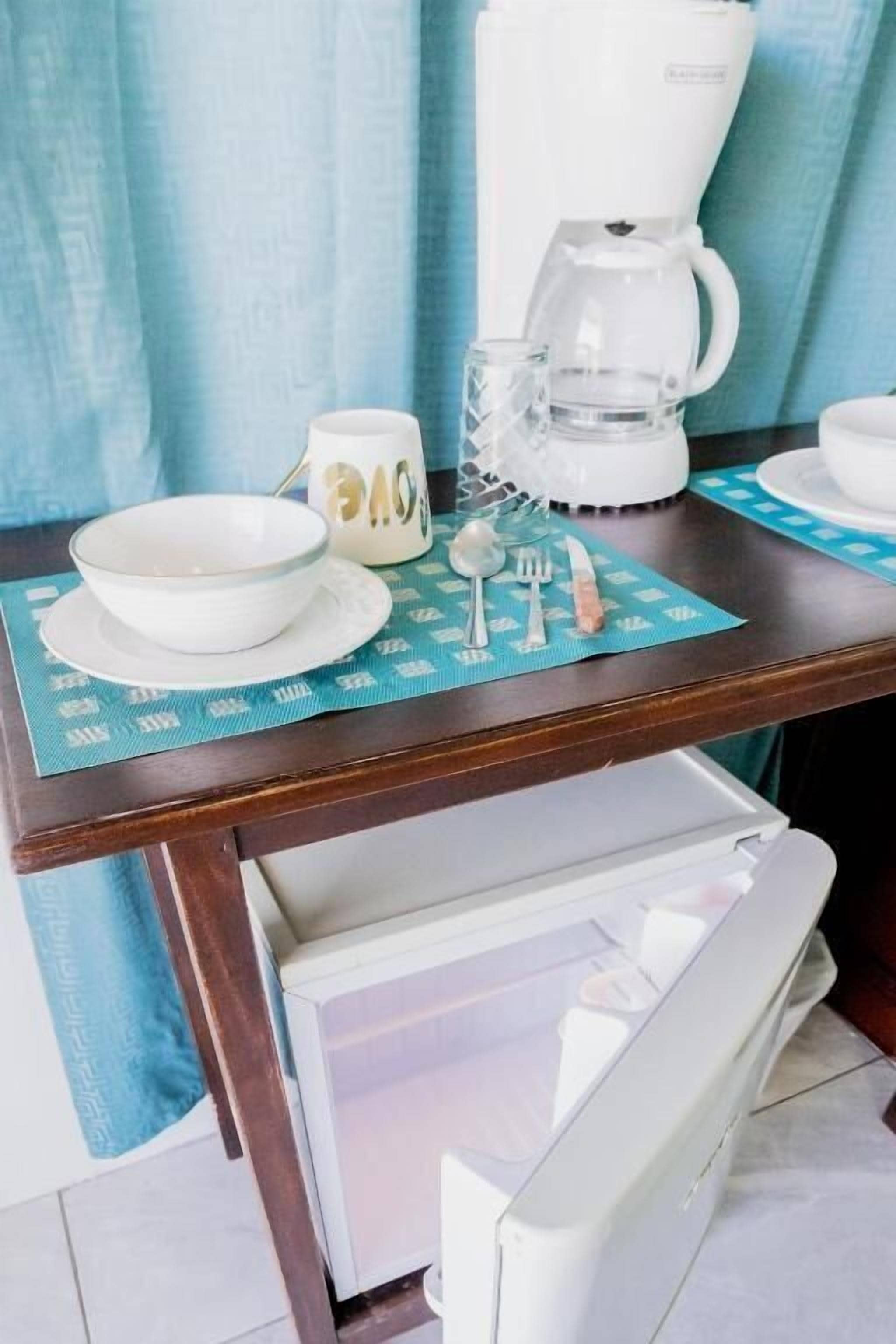 A kitchen counter with a coffee maker, a bowl, a mug, and utensils on a placemat.