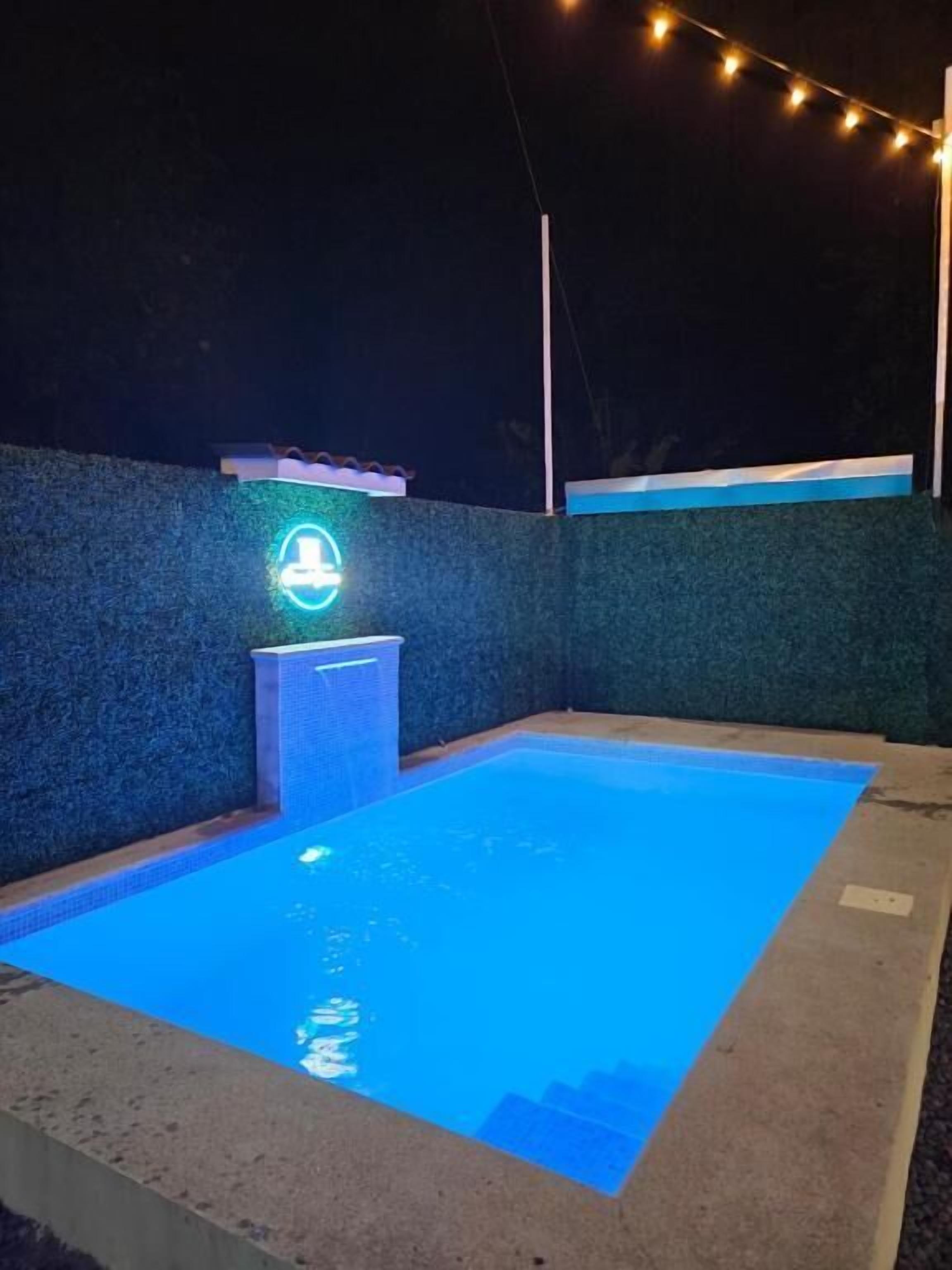 A swimming pool with a neon sign and string lights.