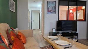 A modern living room with a sofa, a dining table set for two, a television, and a framed picture on the wall. - Picasso | Terrace & Garden | Honfleur City Center (Honfleur)