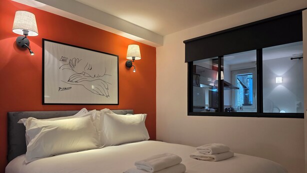 A hotel room with a bed, two wall-mounted lamps, a framed artwork, and a window with a view of the interior. - Picasso | Terrace & Garden | Honfleur City Center (Honfleur)