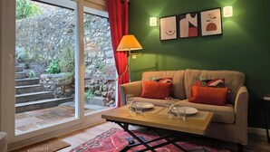 A cozy living room with a sofa, a coffee table, and a view of a stone wall and greenery outside. - Picasso | Terrace & Garden | Honfleur City Center (Honfleur)