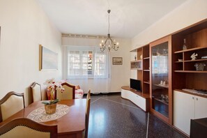 A dining area with a wooden table, chairs, and a chandelier. There is a television on a wooden cabinet and a window with sheer curtains. - Casa Aladino By Arenzanohost (Arenzano)