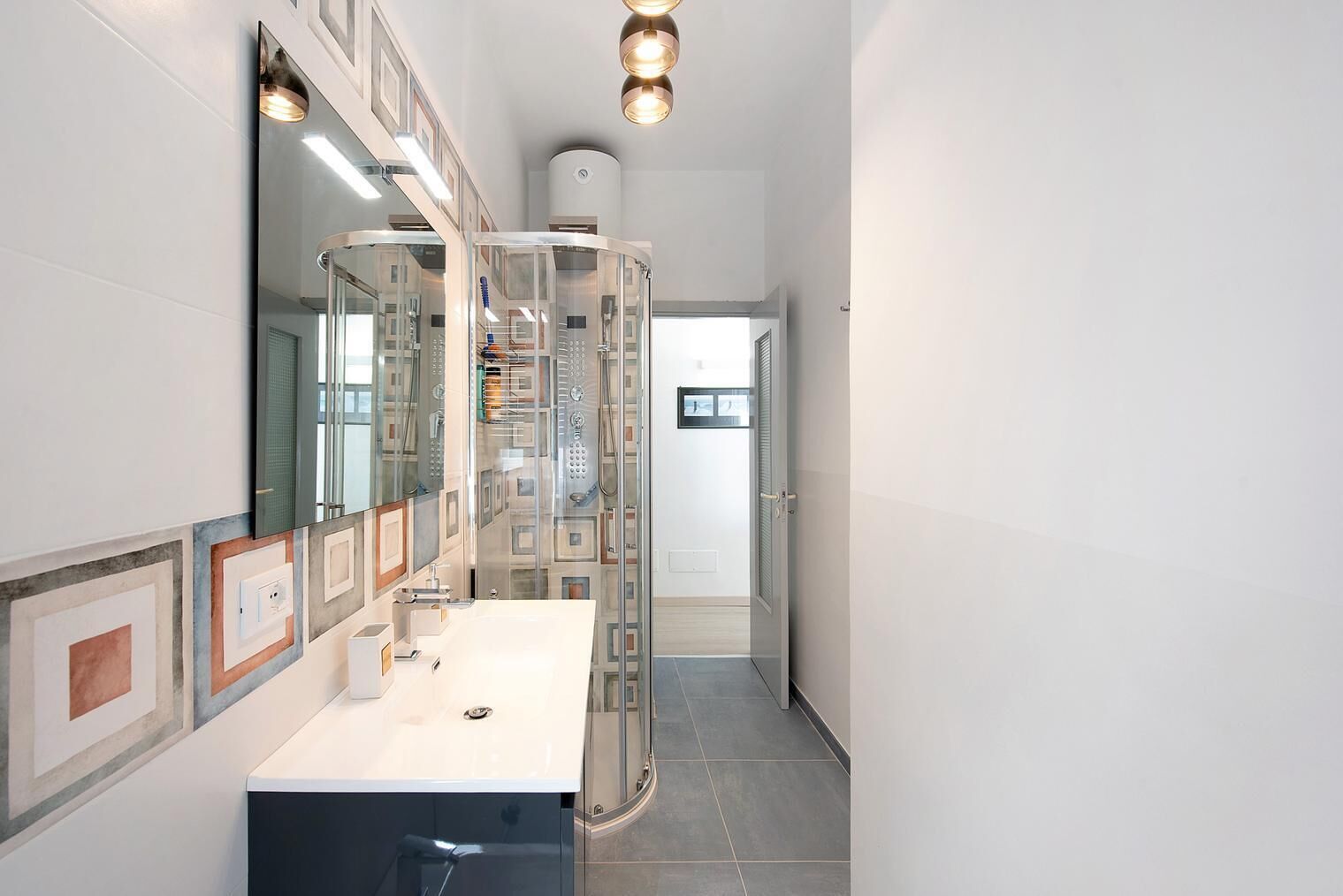 Ein modernes Badezimmer mit einem großen Spiegel, einem weißen Waschbecken und einer Duschkabine aus Glas.