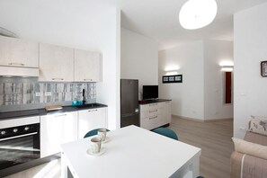 A modern kitchen with white cabinets, a black refrigerator, and a dining area with a white table and chairs. - Casa Azzurra - One Bedroom Apartment, Sleeps 4 (Arenzano)