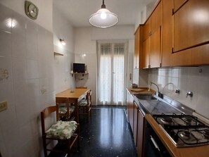 Una cocina compacta con estufa a gas, armarios de madera, una mesa de comedor con sillas y un televisor en un estante.