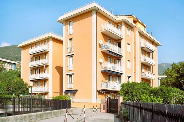 A multi-story residential building with balconies, a gated entrance, and a surrounding fence.