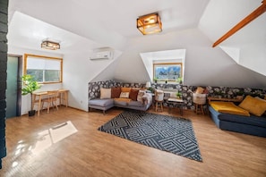 Avoin, loft-tyylinen huone, jossa on ruokailutila, sohva, pieni pöytä ja ikkuna, josta on näkymä.