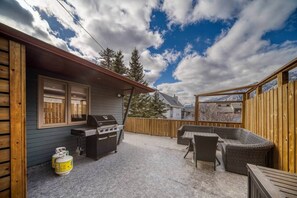A covered patio with a grill, wicker furniture, and a view of mountains.