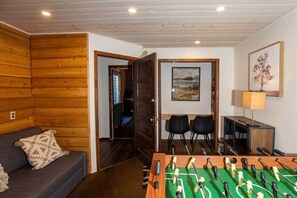 A room with a sofa, a foosball table, a desk with a lamp, and two chairs.