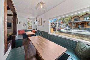 A cozy interior with wooden benches and tables, a large window with a view of a wooden building outside.