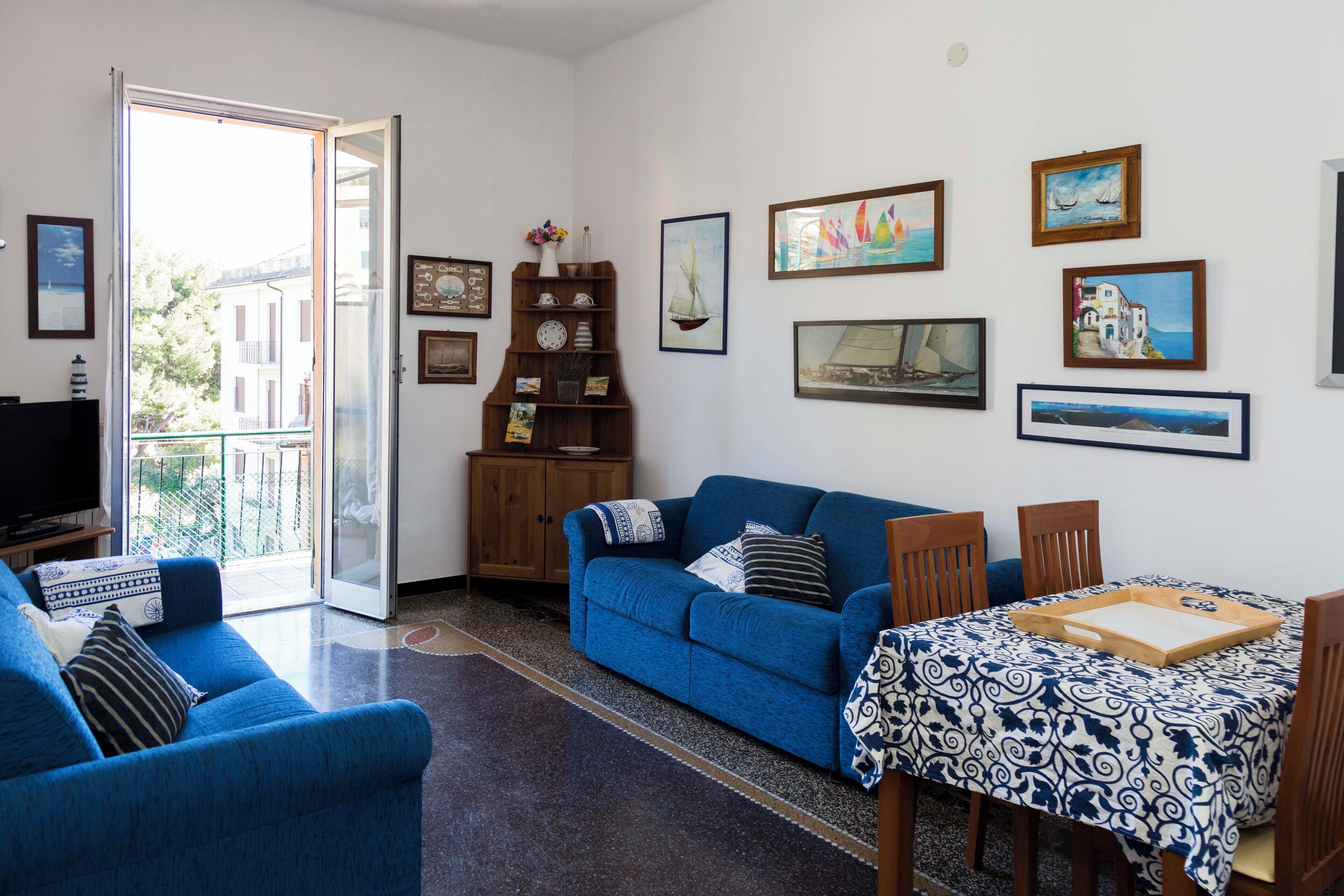 Ein Wohnzimmer mit einem blauen Sofa, einem Esstisch mit Tablett und einem Fernseher auf einem Schrank.