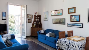 Una sala de estar con un sofá azul, una mesa de comedor con una bandeja y un televisor sobre un mueble.