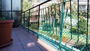 Un balcón con barandilla metálica verde, una planta en maceta y una vista de un puente y montañas al fondo.