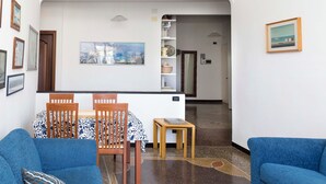 Una sala de estar moderna con un sofá azul, un comedor con mesa y sillas, y un pasillo que conduce a otra habitación.