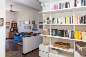 Ein Wohnzimmer mit einem blauen Sofa, einem weißen Bücherregal voller Bücher und einem Deckenventilator.