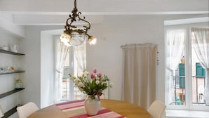 A dining area with a round table, chairs, a vase with flowers, a chandelier, and a view of the outside through large windows. - Casa Fiordaliso - One Bedroom Apartment, Sleeps 4 (Arenzano)
