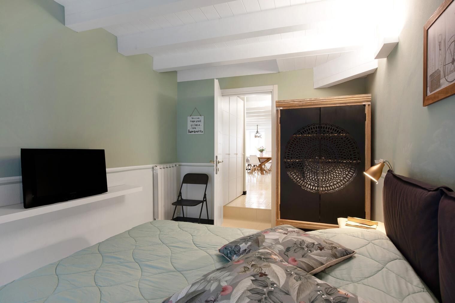 Un dormitorio con cama, televisión, una silla y una puerta que da a un comedor.