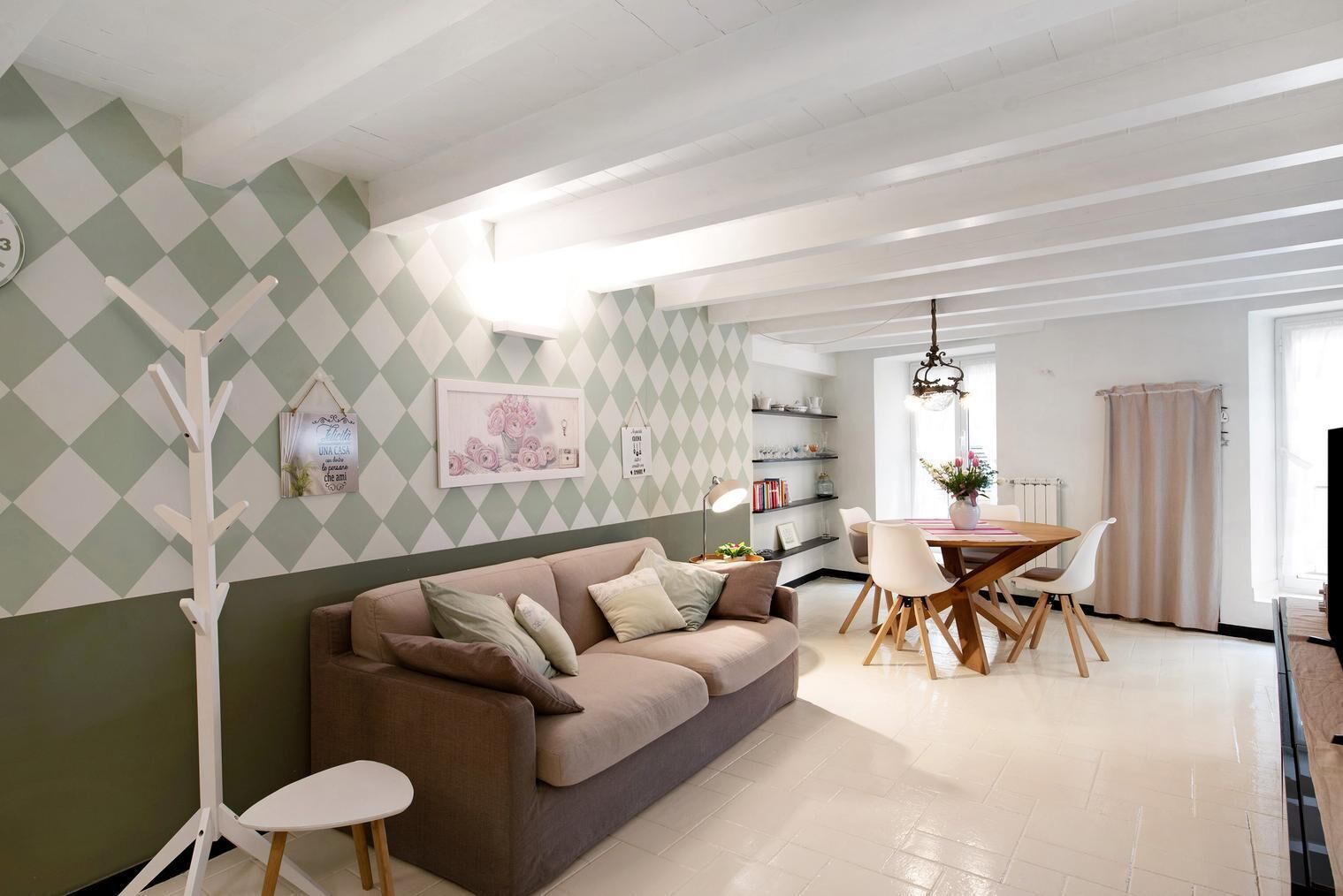 A living room with a sofa, a dining table with chairs, a coat rack, and a bookshelf.