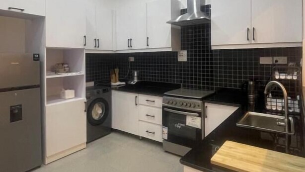 Una cucina moderna con mobili bianchi, una cappa in acciaio inossidabile, forno integrato e piano di lavoro nero.