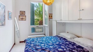 Ein Schlafzimmer mit Bett, einem Fenster mit Rollläden, einer Pendelleuchte und einem weißen Kleiderschrank.