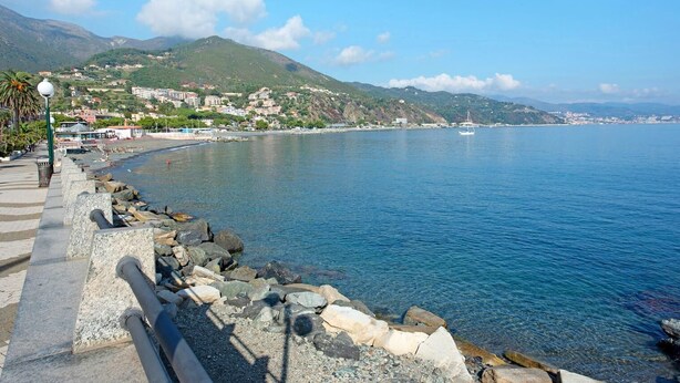 Una passeggiata lungomare con ringhiera in pietra, vista libera sul mare e edifici sullo sfondo.