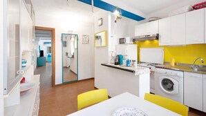 Una cucina moderna con mobili bianchi, un forno a microonde, un piano cottura e una lavatrice. C'è un'area pranzo con tavolo e sedie.