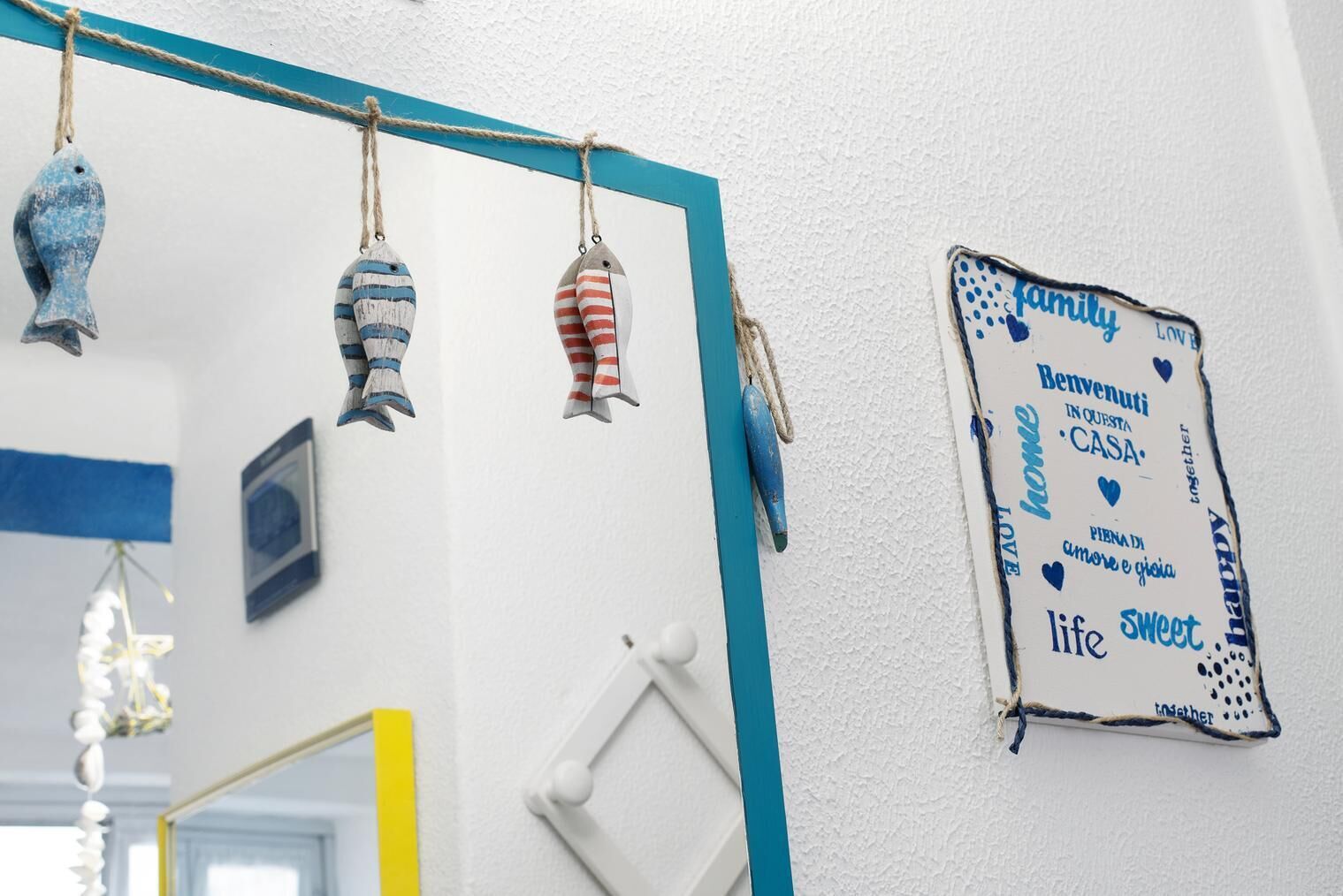 A wall with a blue and white sign that reads "Benvenuti in questa casa" and decorative fish-shaped ornaments.