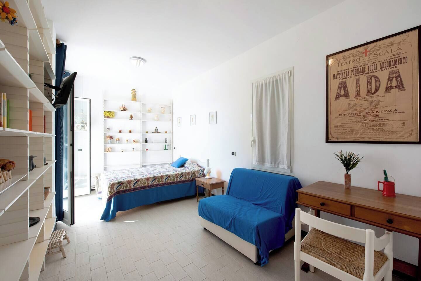 Une chambre à coucher avec un lit, un bureau, une chaise, une bibliothèque et une fenêtre.