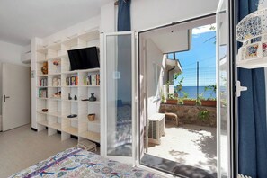 Un dormitorio con un ventanal grande, una cama con colcha estampada, una estantería blanca y vista al mar.