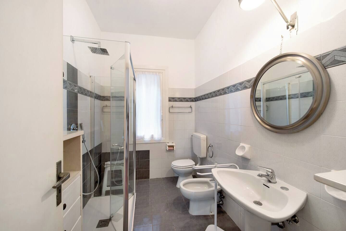 A modern bathroom with a glass-enclosed shower, a toilet, bidet, and a sink with a mirror.