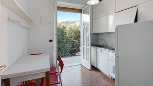 A compact kitchen with white cabinets, a sink, and a dining area with a table and chairs. - Casa Olivette - Two Bedroom Apartment, Sleeps 5 (Arenzano)