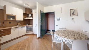 Una cucina compatta con elettrodomestici moderni, una zona pranzo con tavolo e sedie, e un piccolo tavolo da pranzo con tovaglia fantasia.
