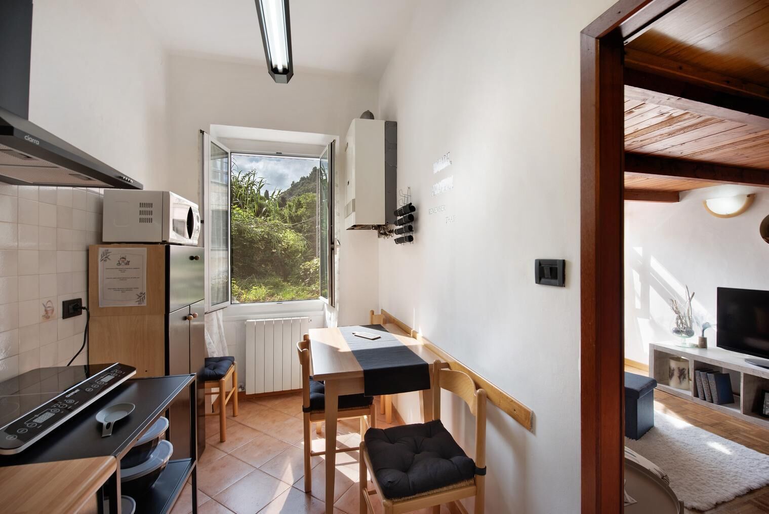 A compact kitchen with a dining area, a built-in oven, a microwave, and a window with a view of greenery.