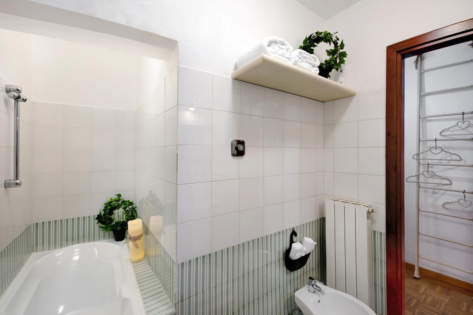 Une salle de bain avec une baignoire, des toilettes et une douche. Il y a des serviettes sur une étagère et une plante accrochée au mur.